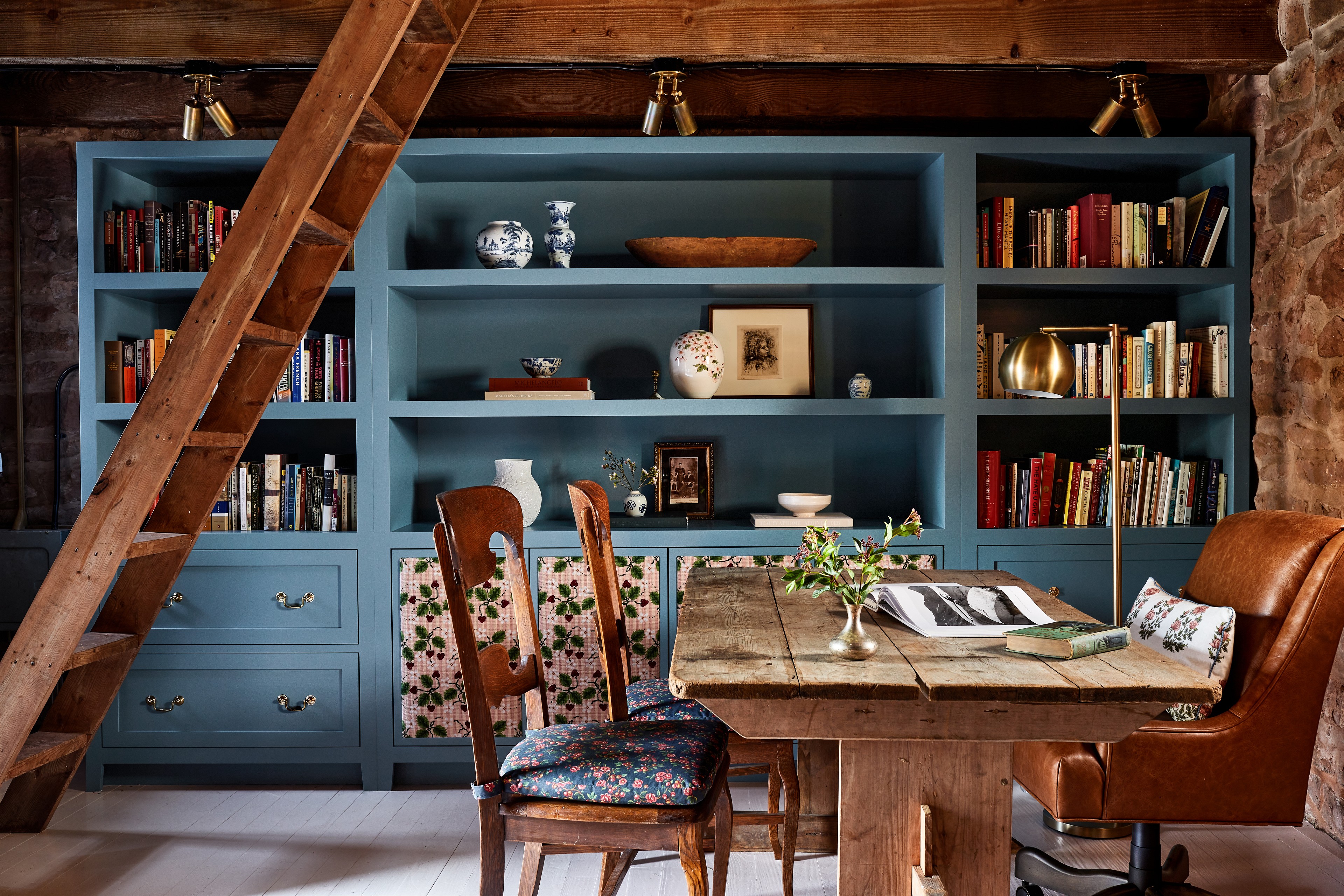 a room with a table, chairs, bookshelves and a ladder