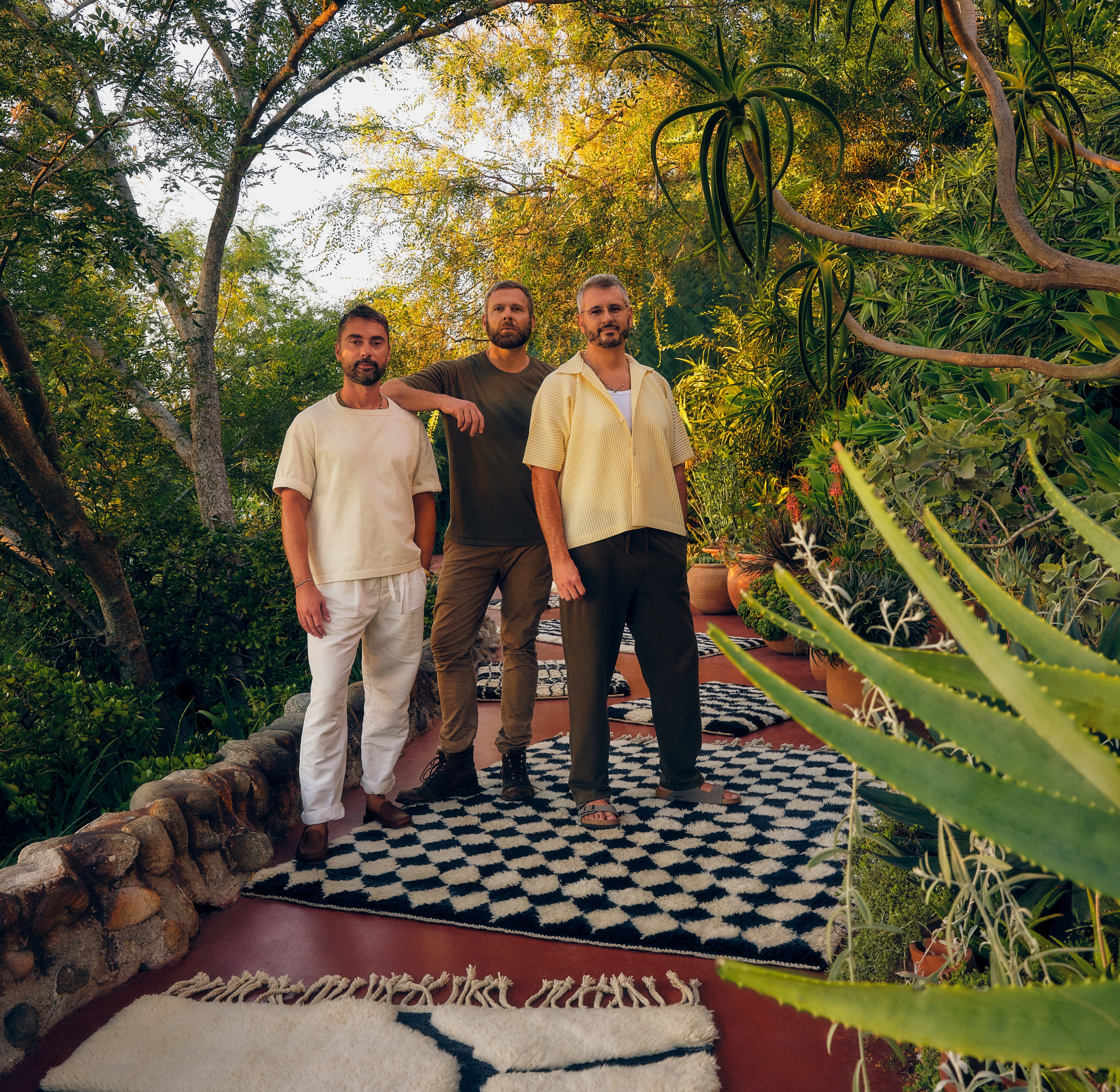 three men standing on a rug in a garden