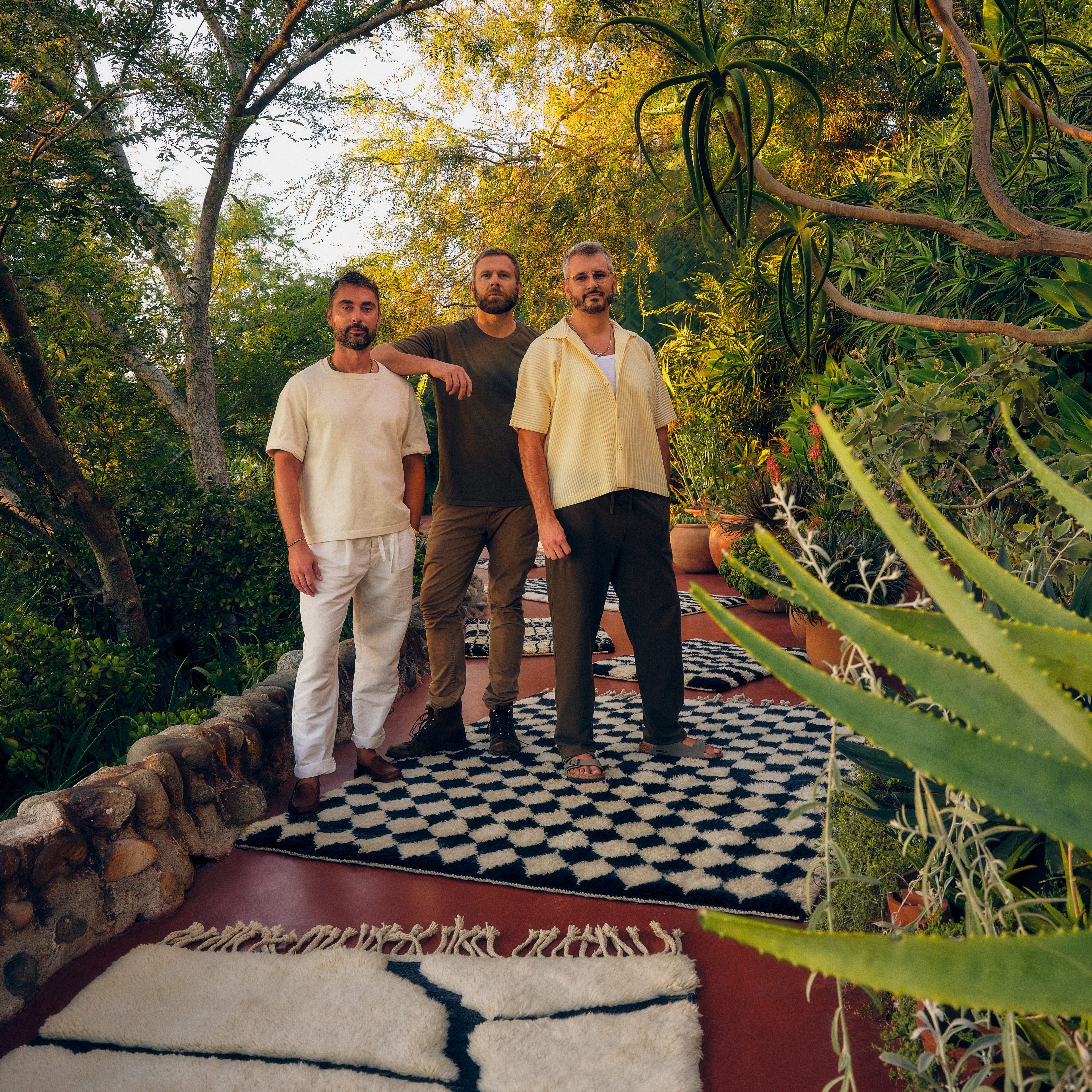 three men standing on a rug in a garden