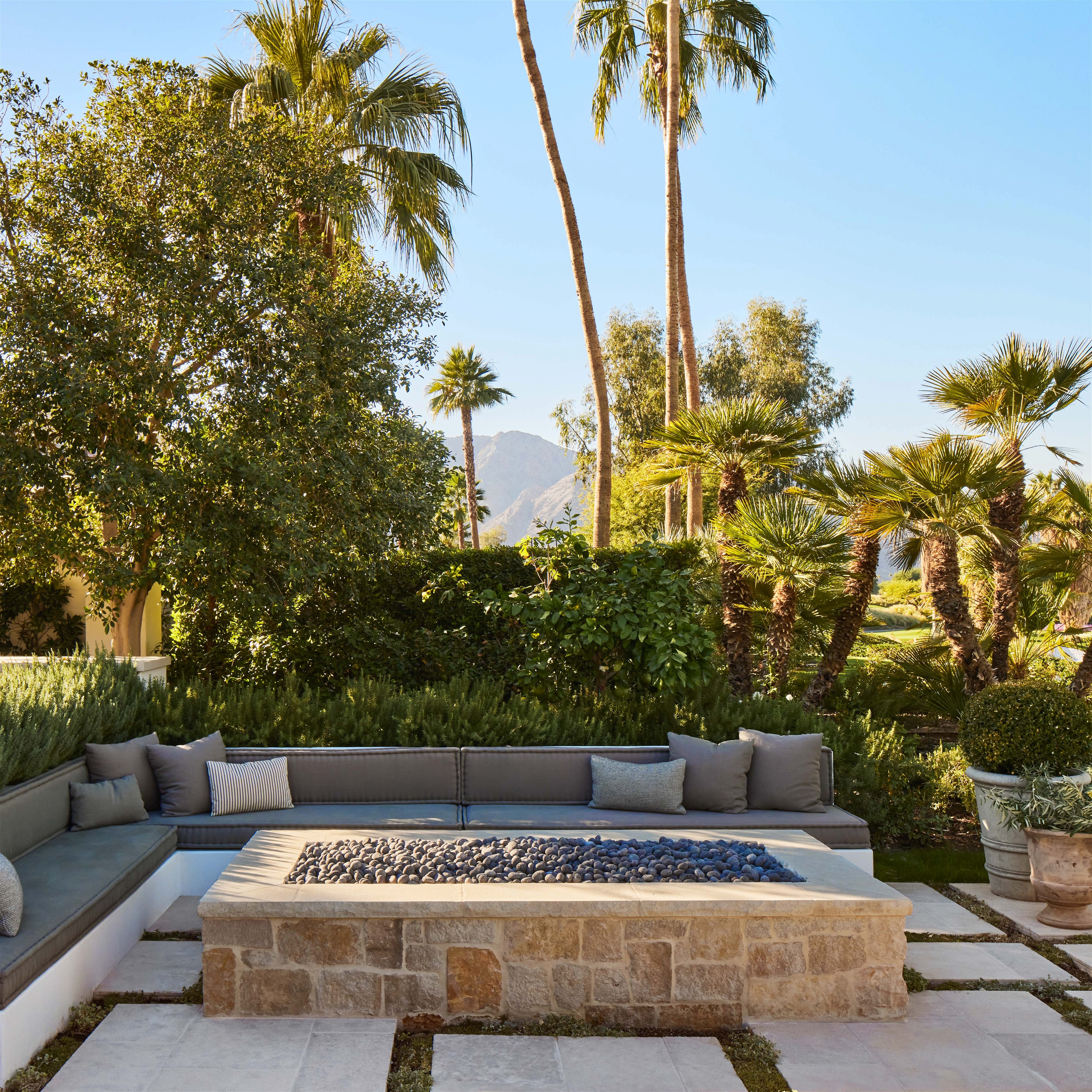 a patio with a fire pit surrounded by palm trees