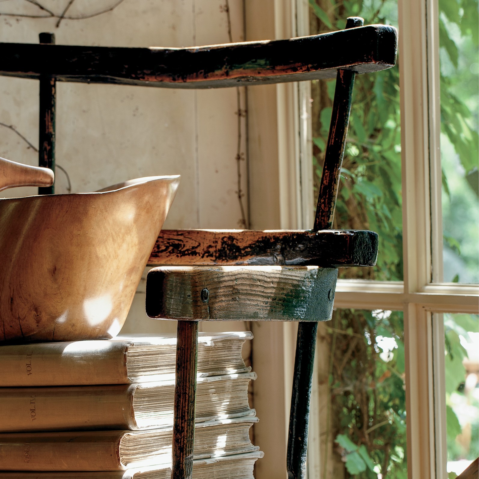 a stack of books sitting on top of a wooden chair next to a window