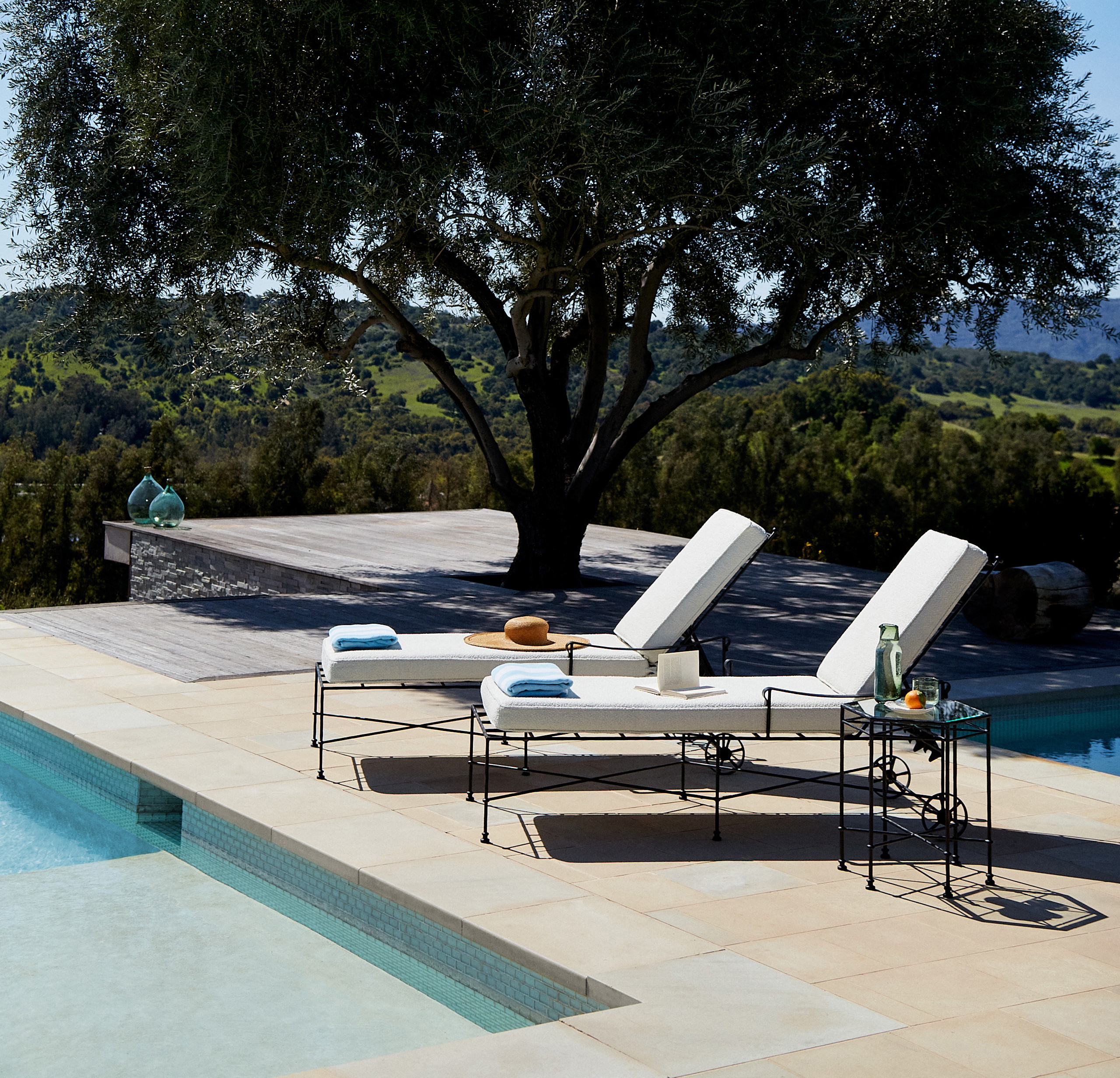 two lounge chairs next to a tree near a swimming pool