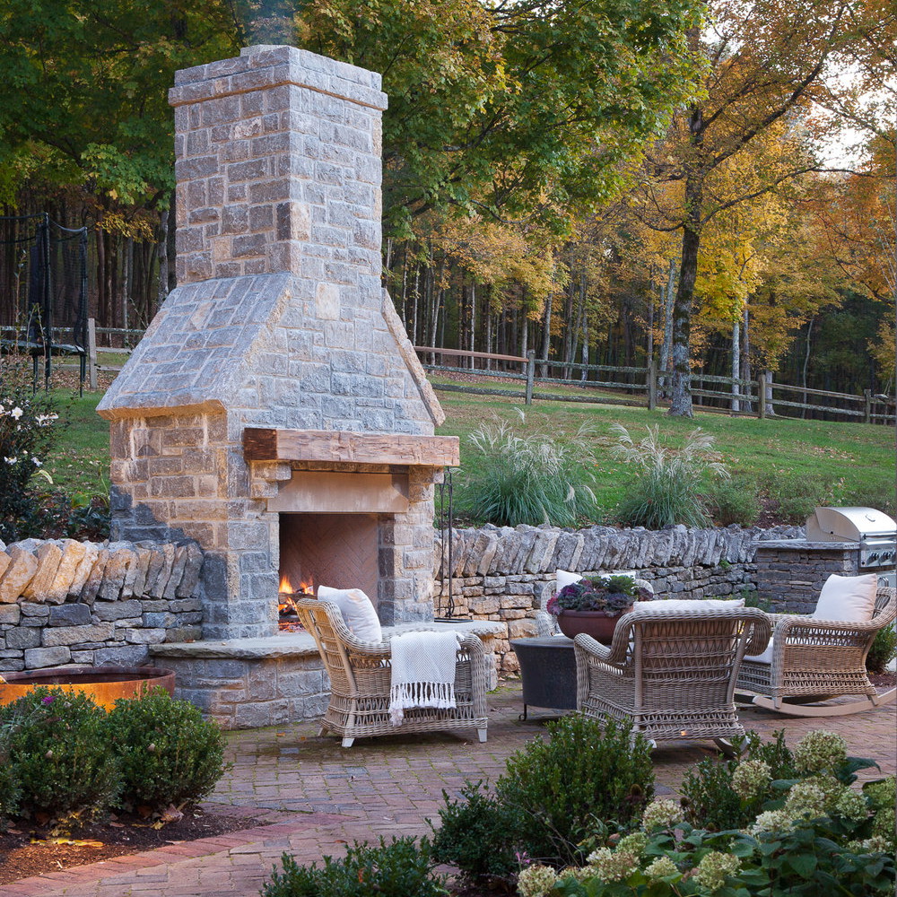 a patio with a fire place surrounded by greenery