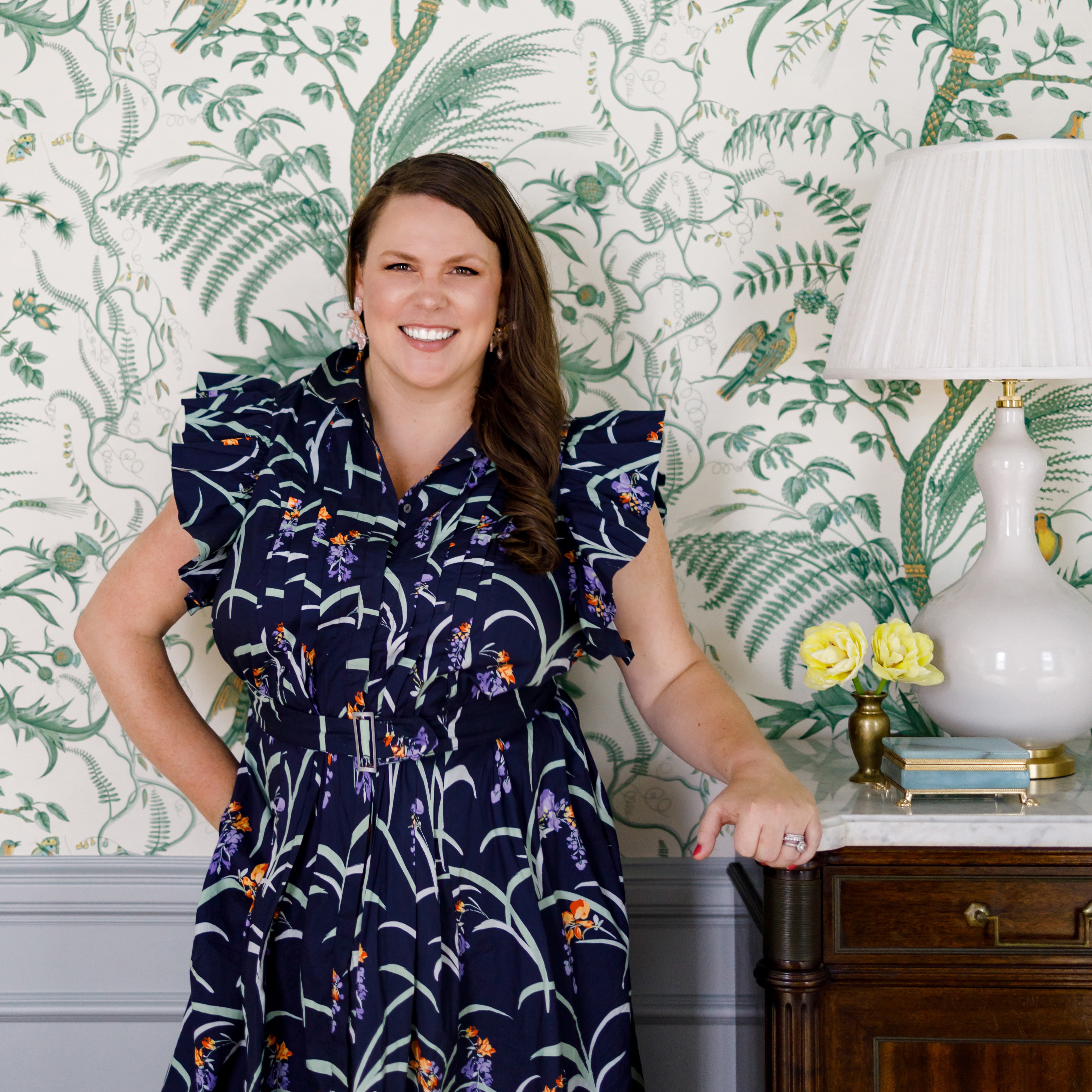 a woman standing in front of a wallpapered wall