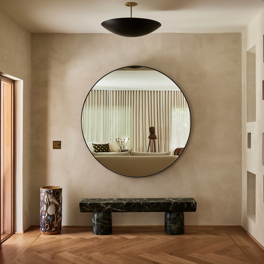 a large round mirror hanging on the wall above a bench