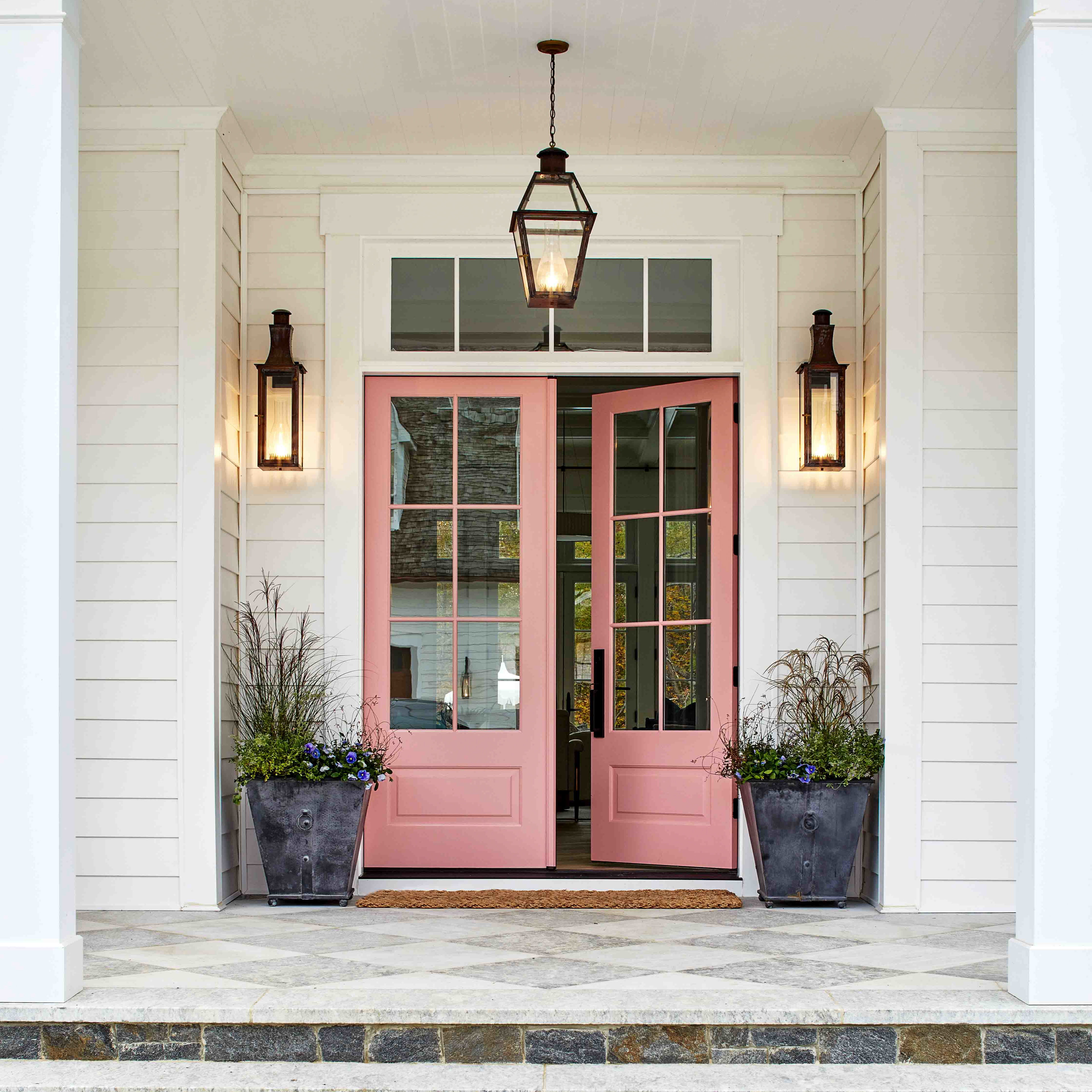 a pink front door with two planters on the steps