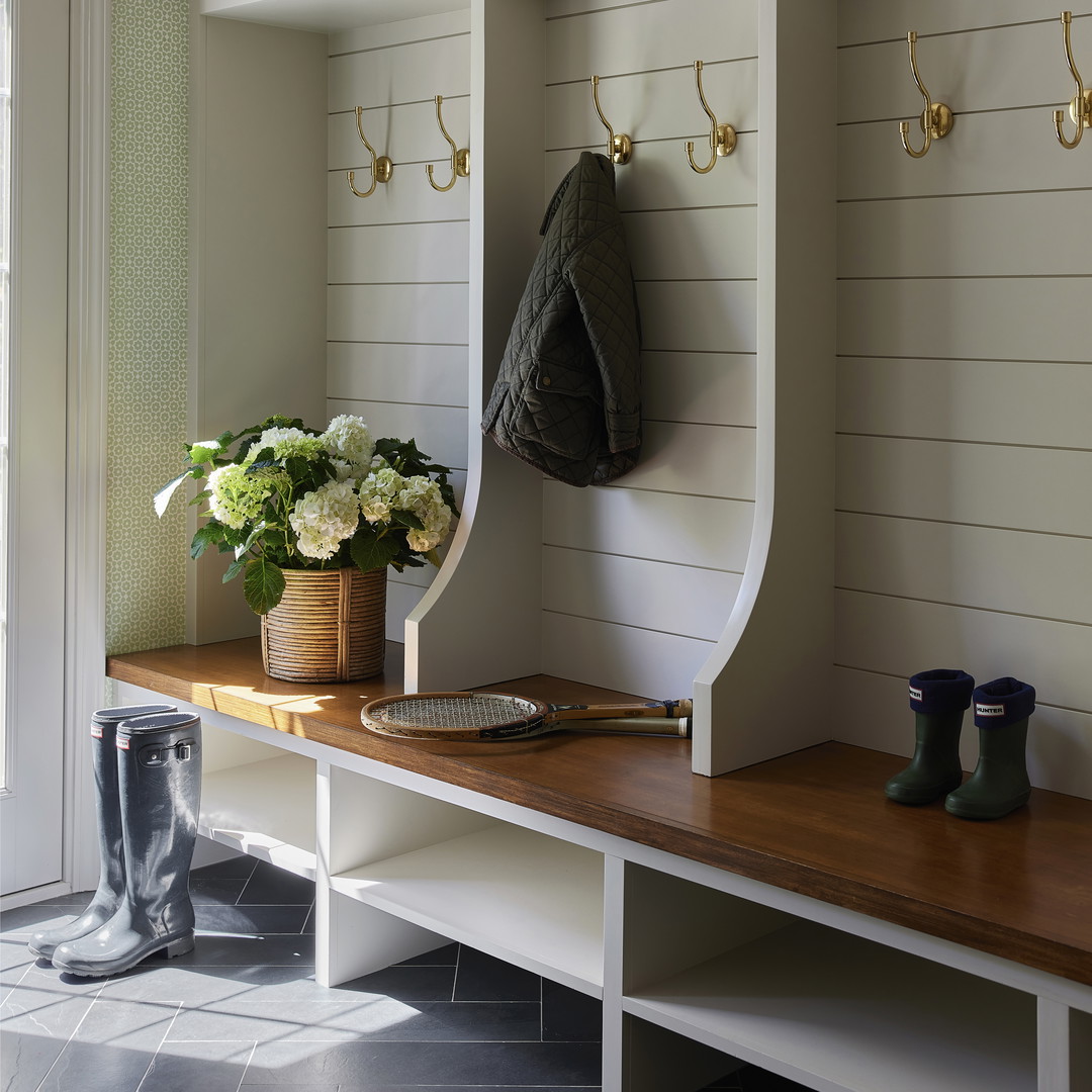 a bench with a coat rack and a vase of flowers