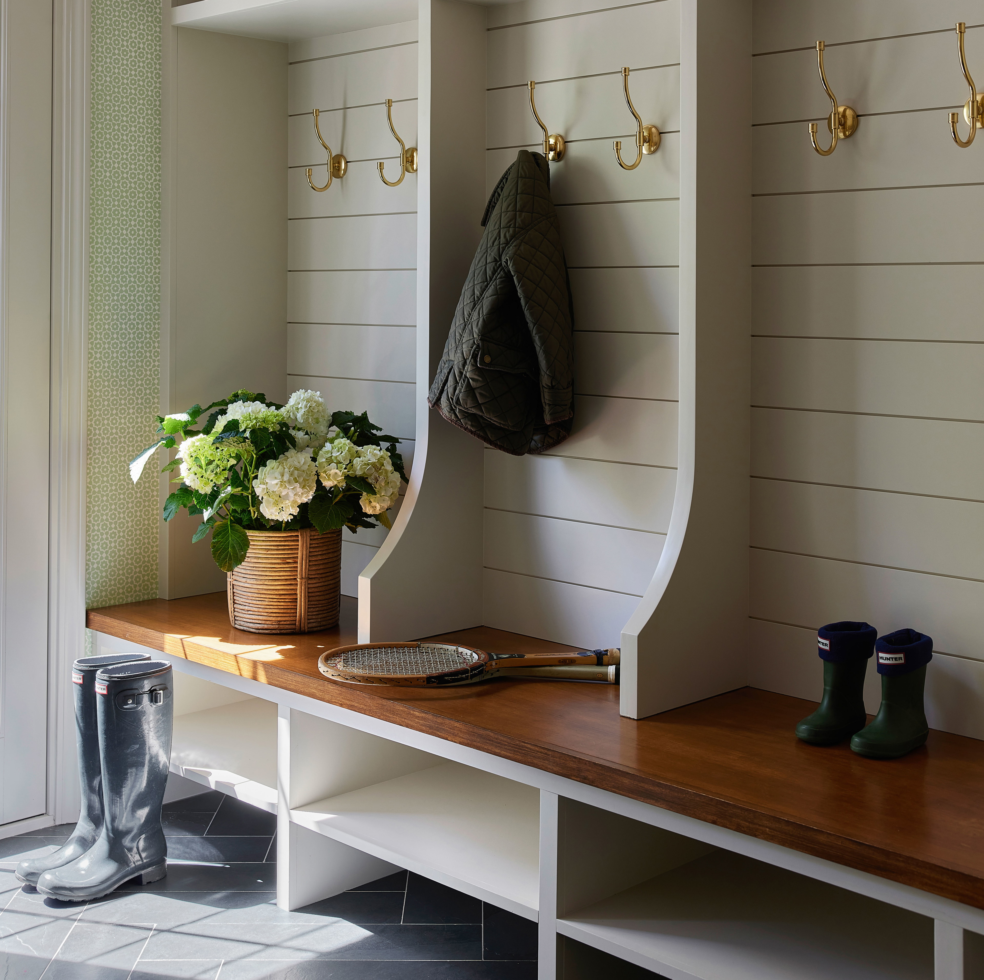 a bench with a coat rack and a vase of flowers