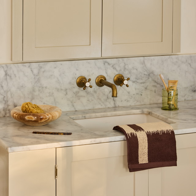 a white kitchen with marble counter tops and gold faucets