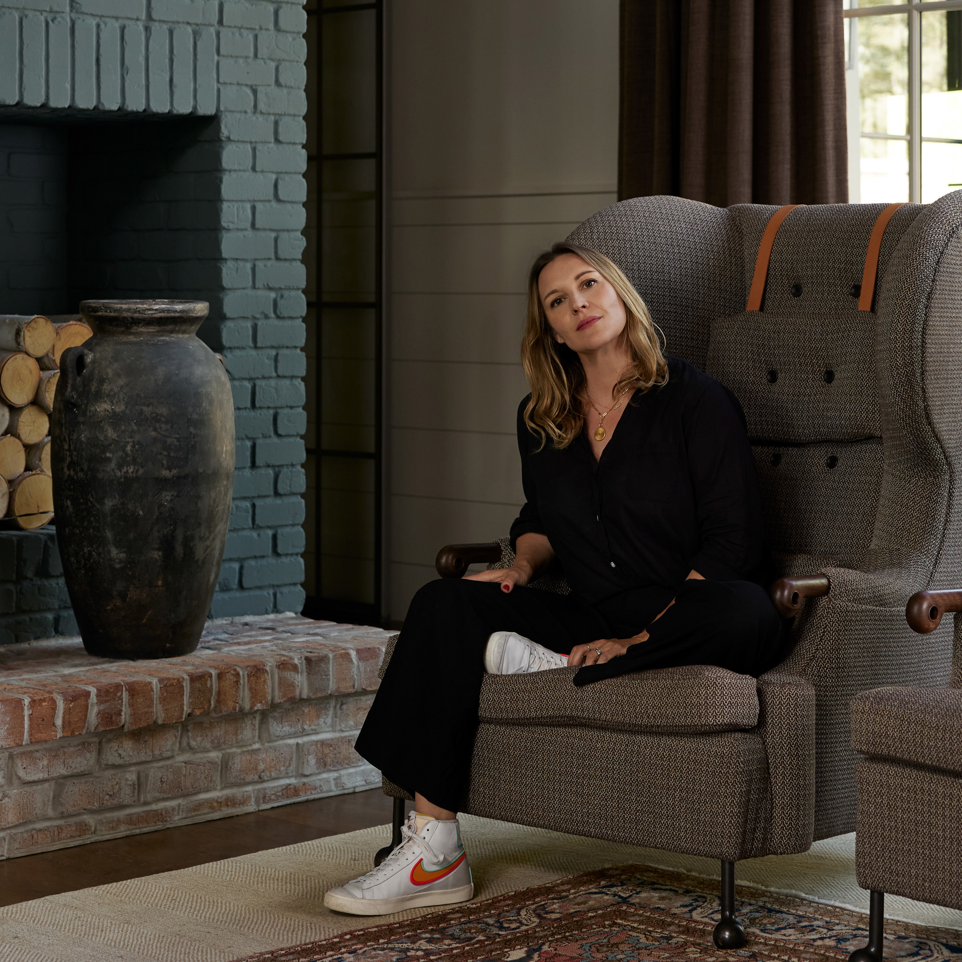 a woman sitting in a chair in front of a fireplace