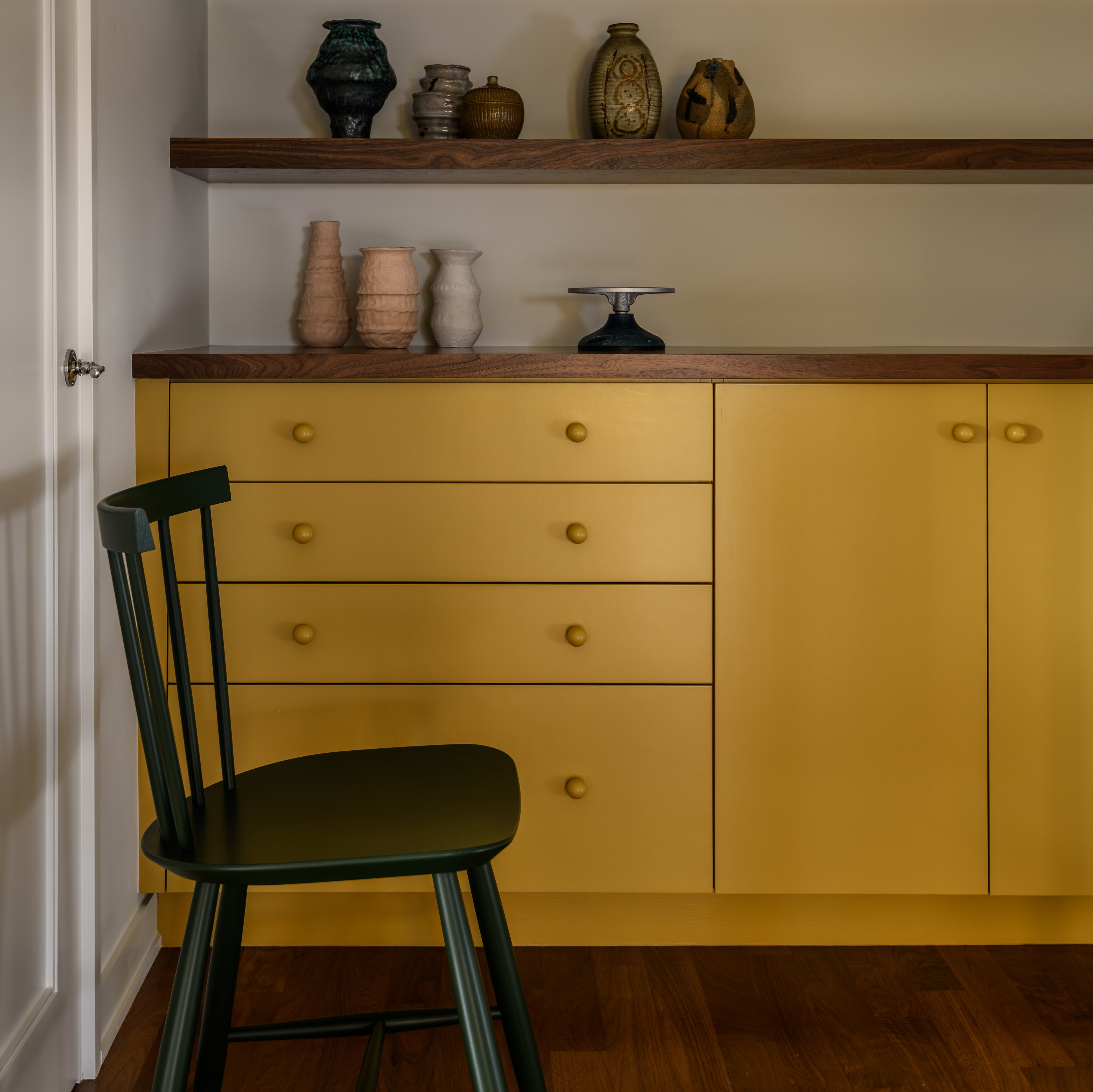 a chair sitting in front of a shelf filled with vases