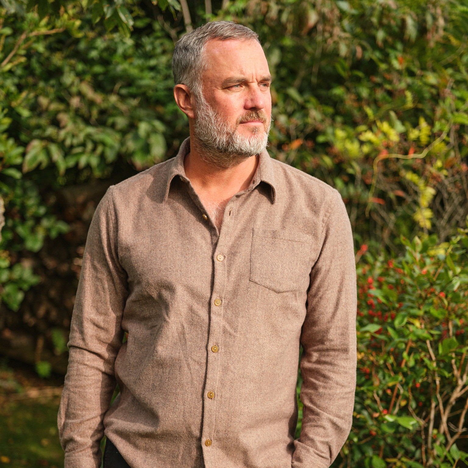 a man with a beard standing in front of a bush