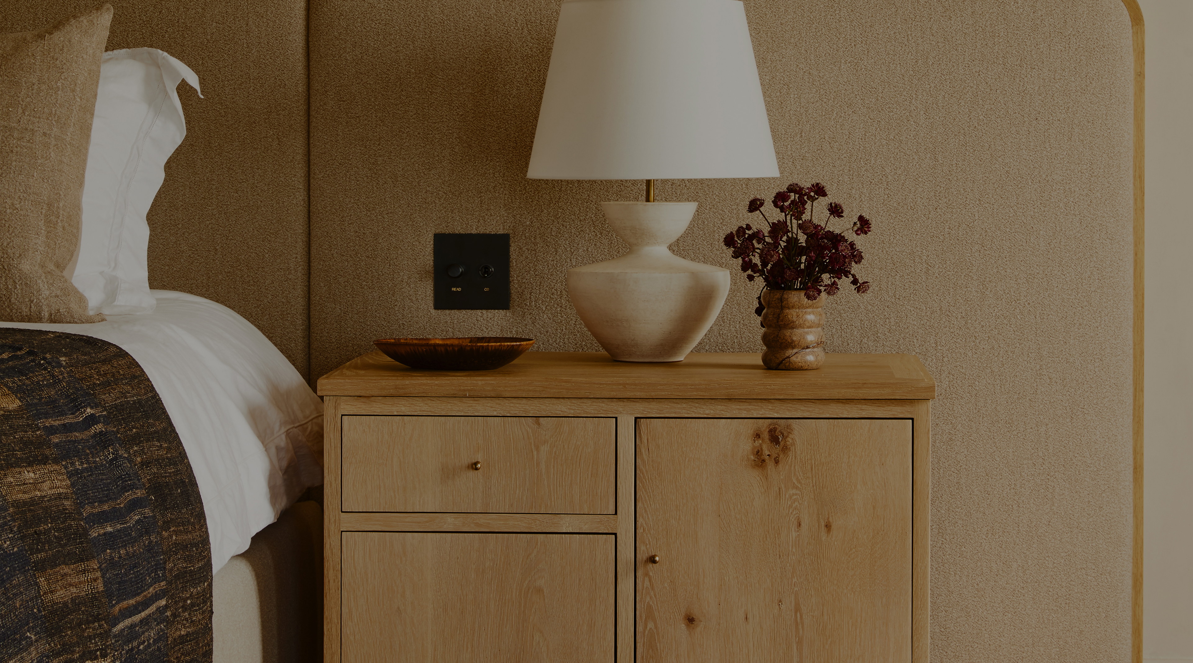 a nightstand with a lamp on top of it next to a bed