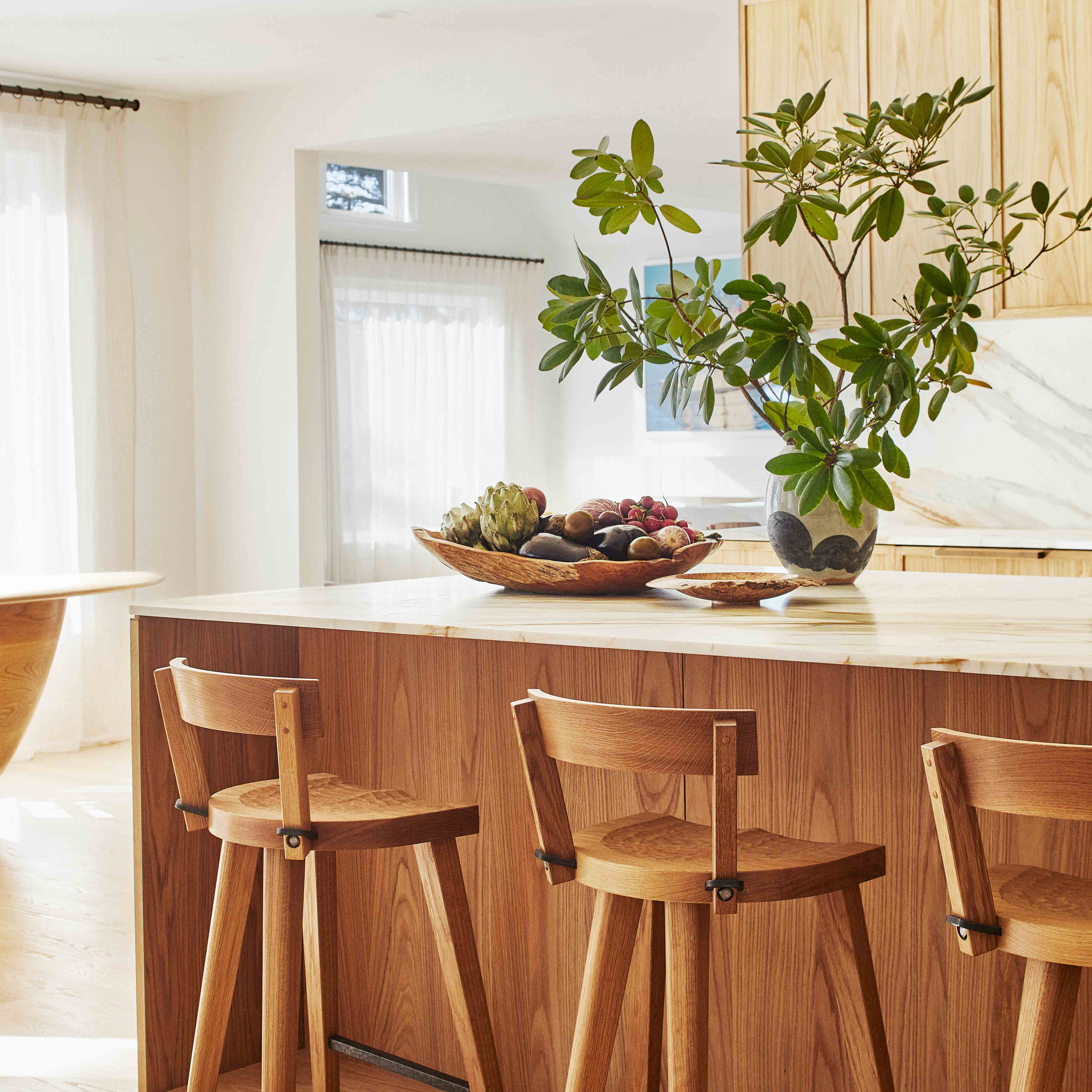 a kitchen with wooden chairs and a bowl of fruit on the counter