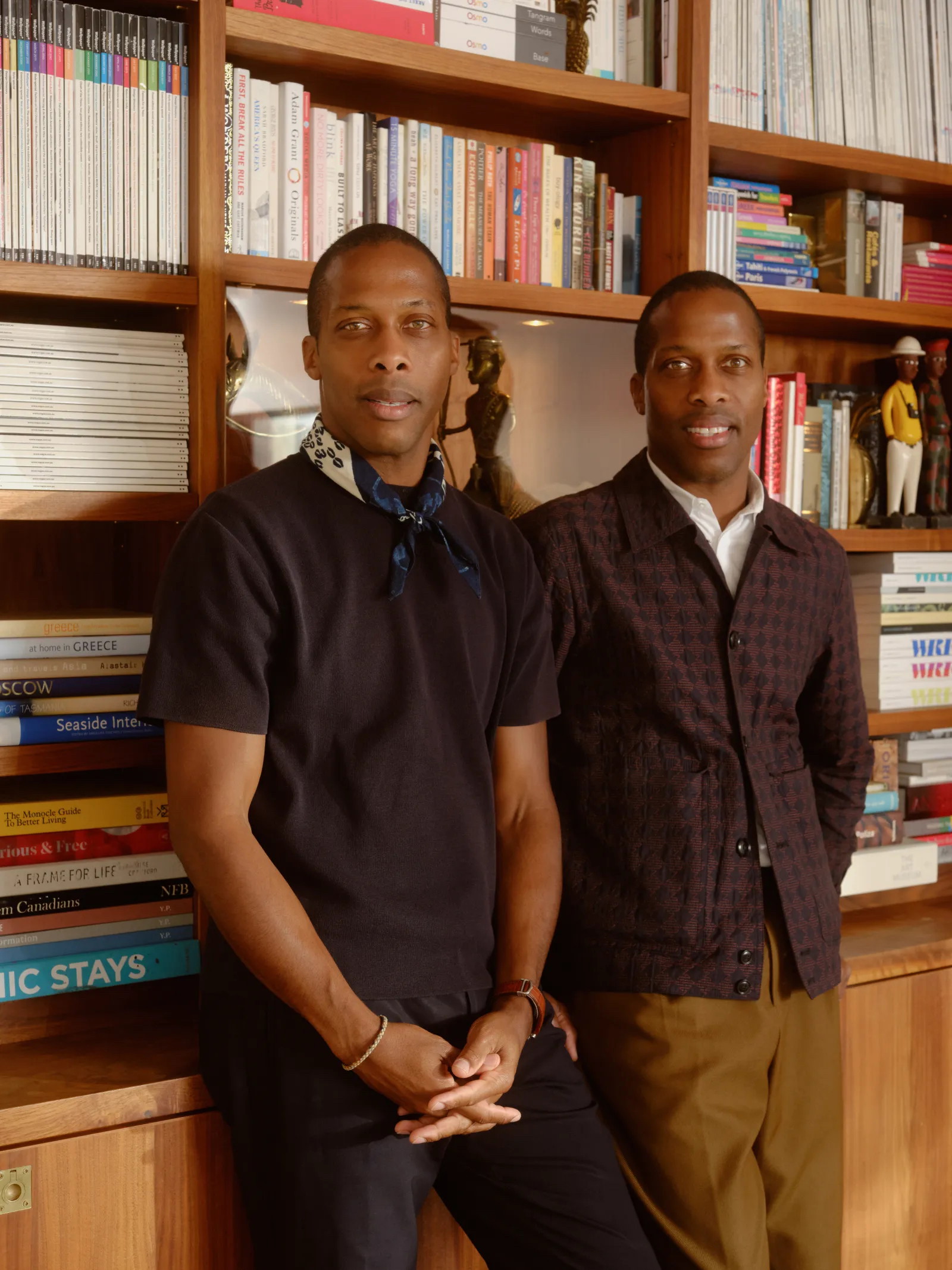 two men standing next to each other in front of a book shelf