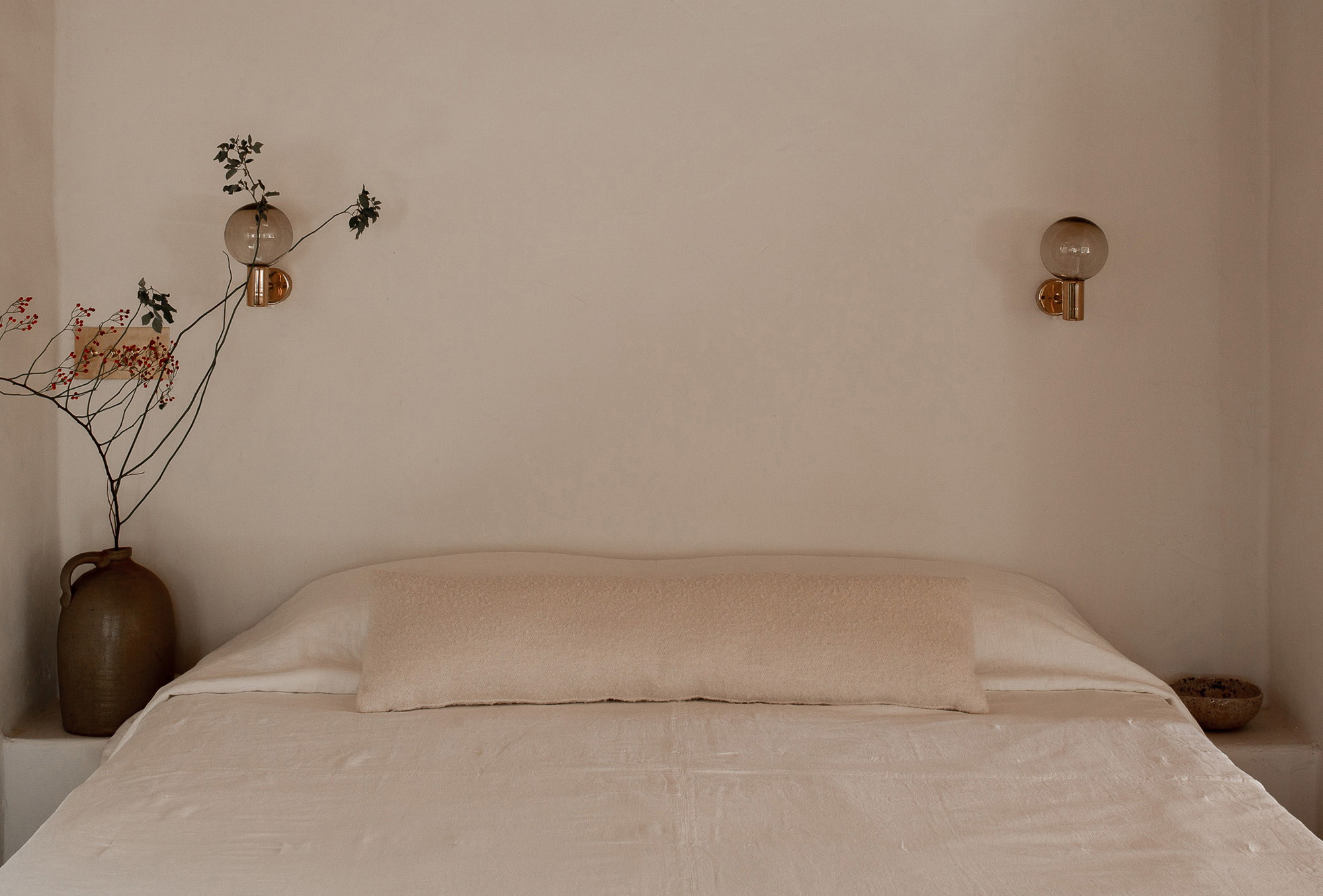 a bed with a white comforter and a vase with flowers