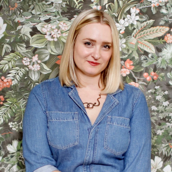 a woman standing in front of a floral wallpaper