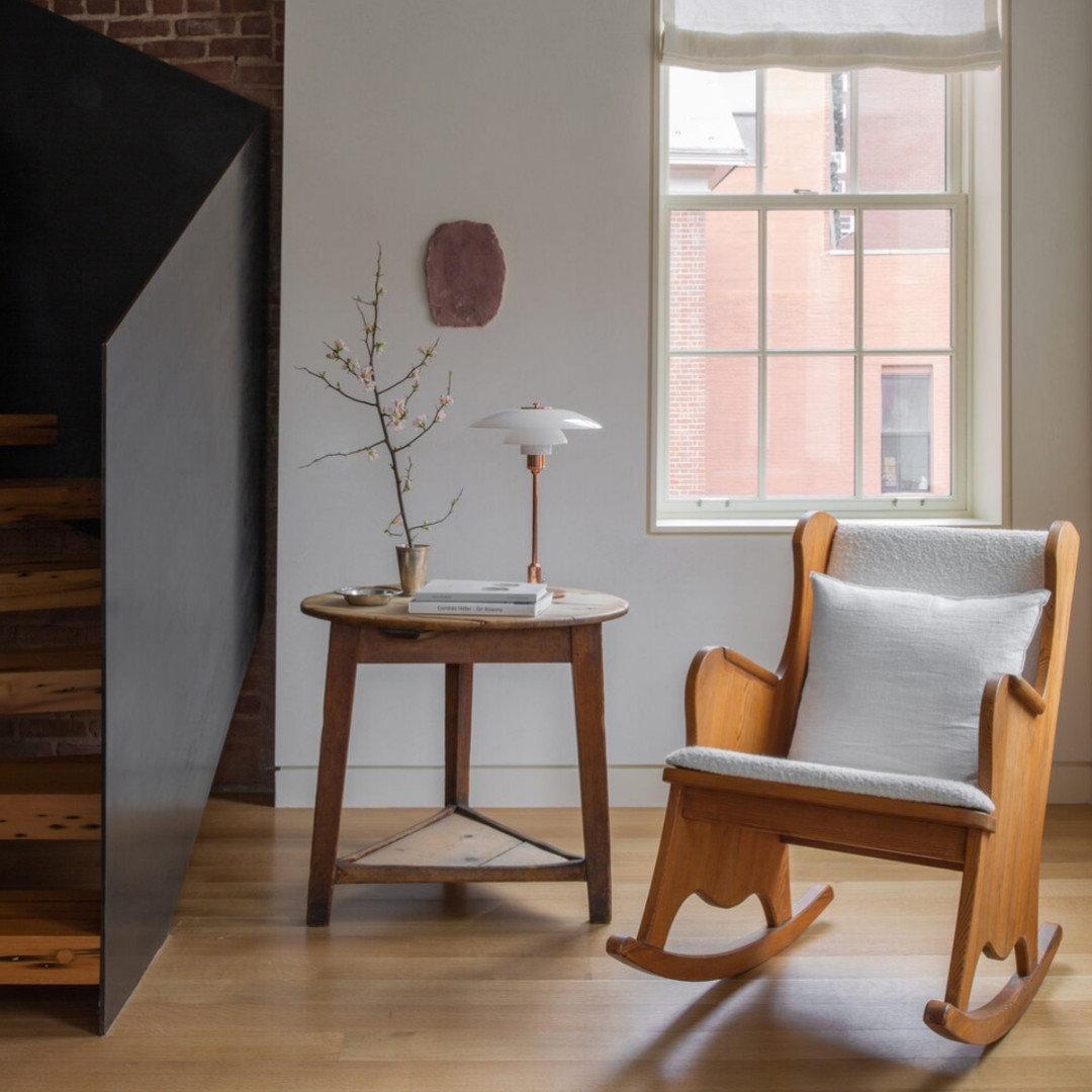 a rocking chair next to a table with a vase on it