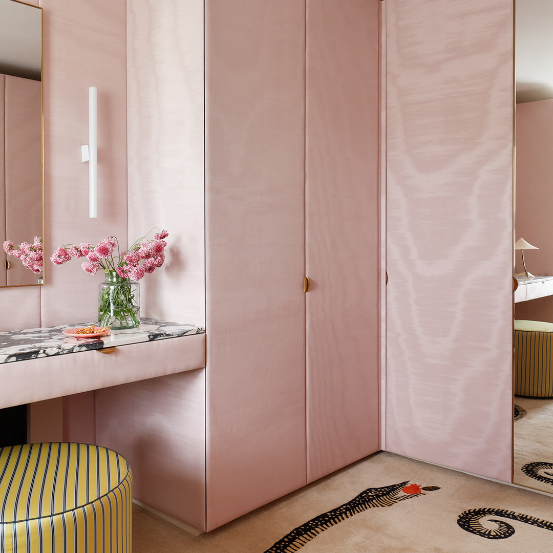 a pink bathroom with a vanity, mirror and stool