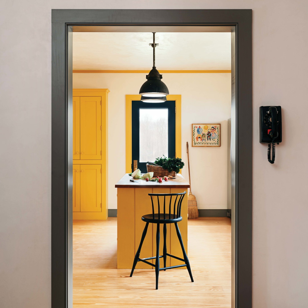 a kitchen with a yellow island and a black bar stool