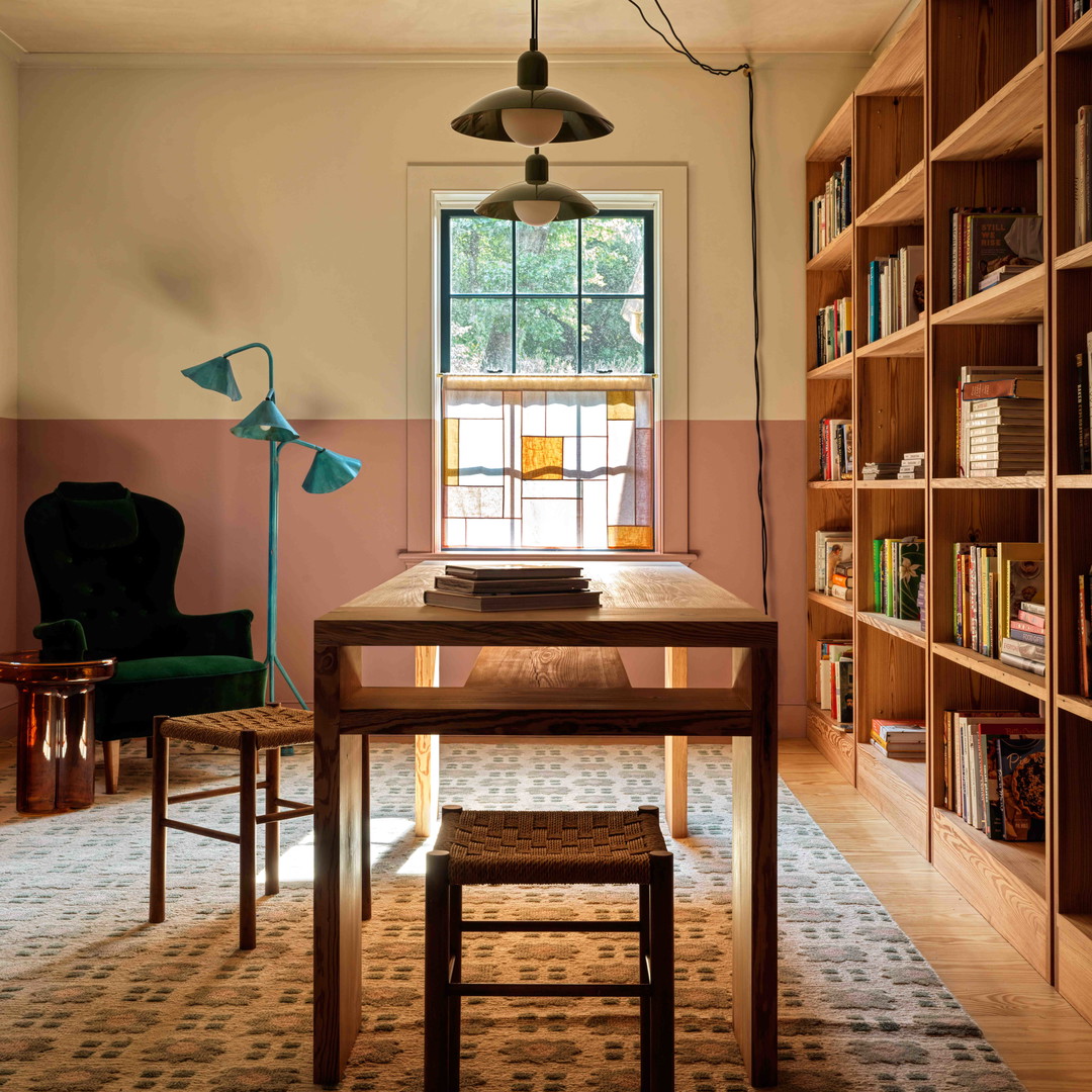 a room with a table, chairs, bookshelves and a lamp