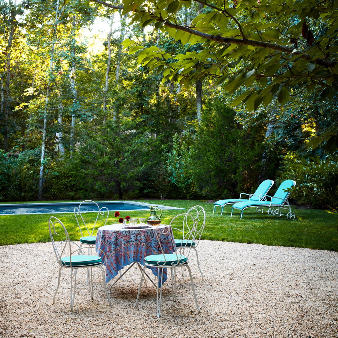 a table and chairs in the middle of a gravel area with a pool in the