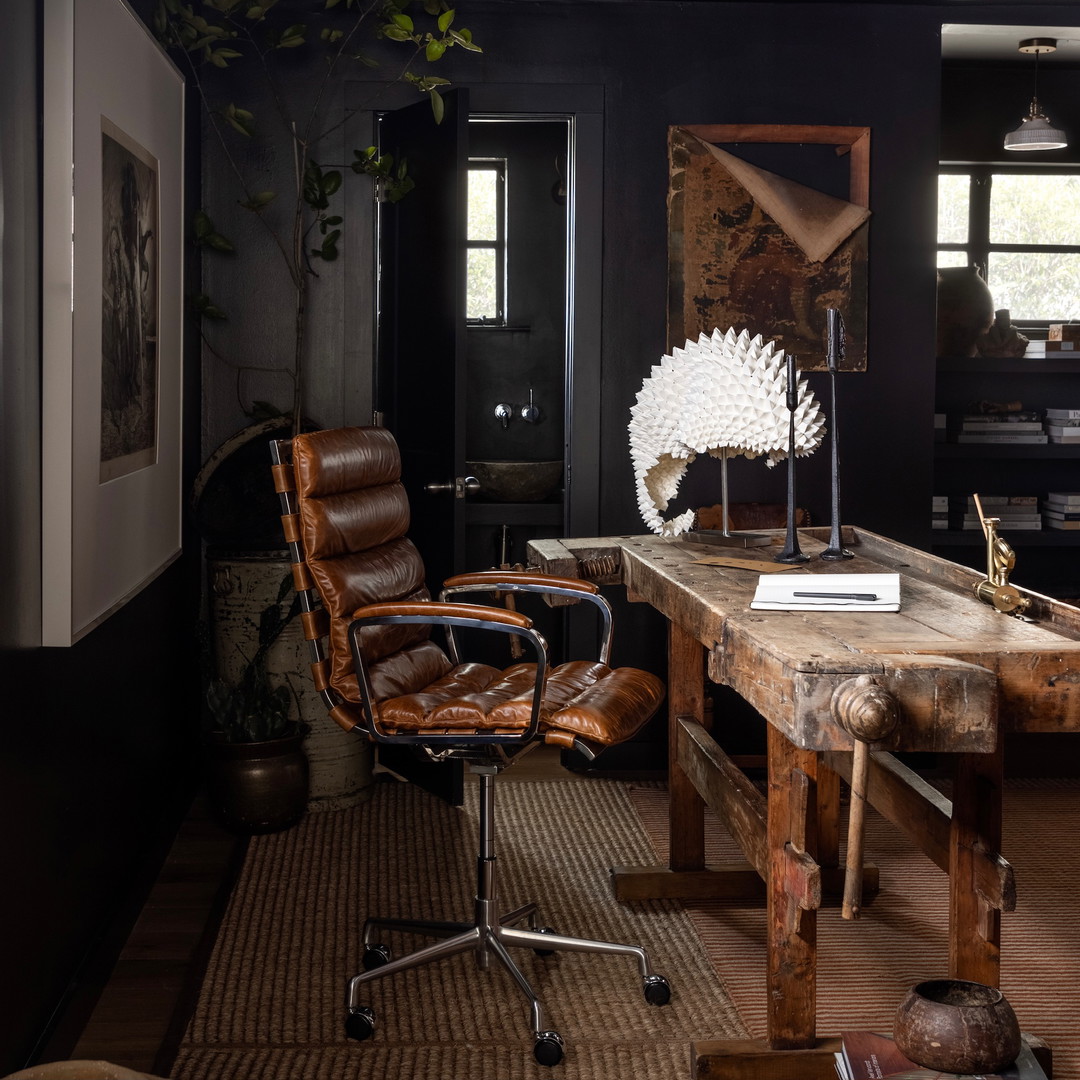 a room with a desk, chair, lamp, and pictures on the wall