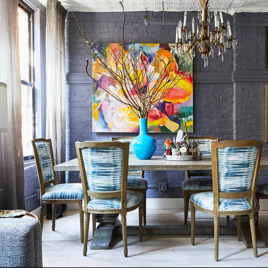 a dining room table with blue chairs and a painting on the wall