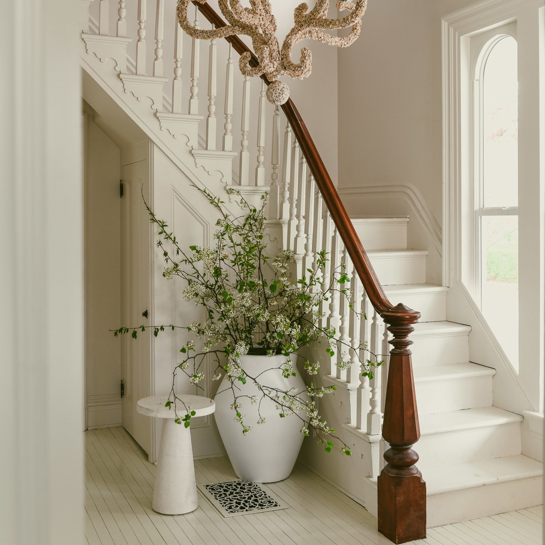 a white vase with a plant in it next to a stair case