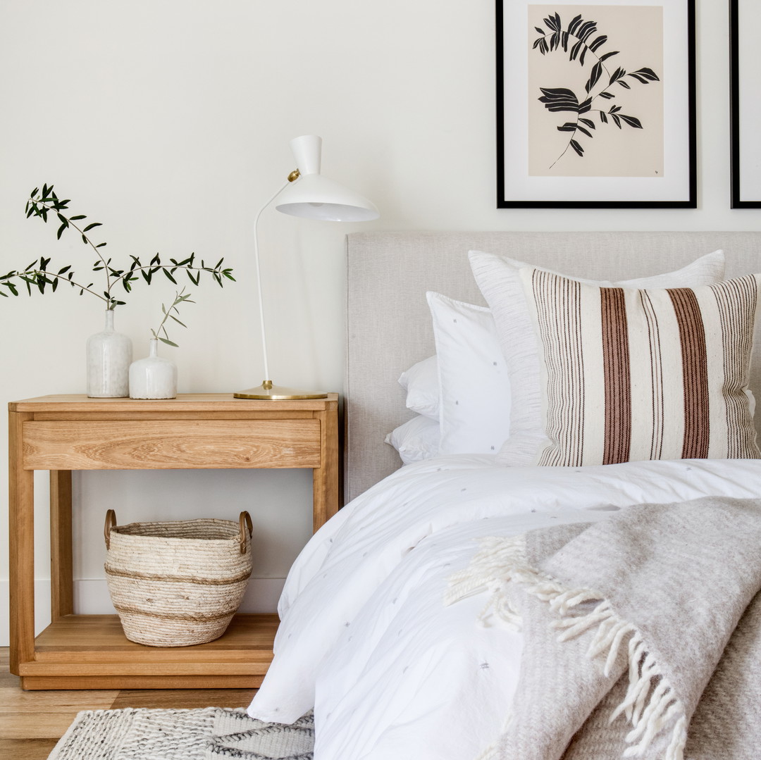 a bed with white sheets and pillows and a wooden night stand