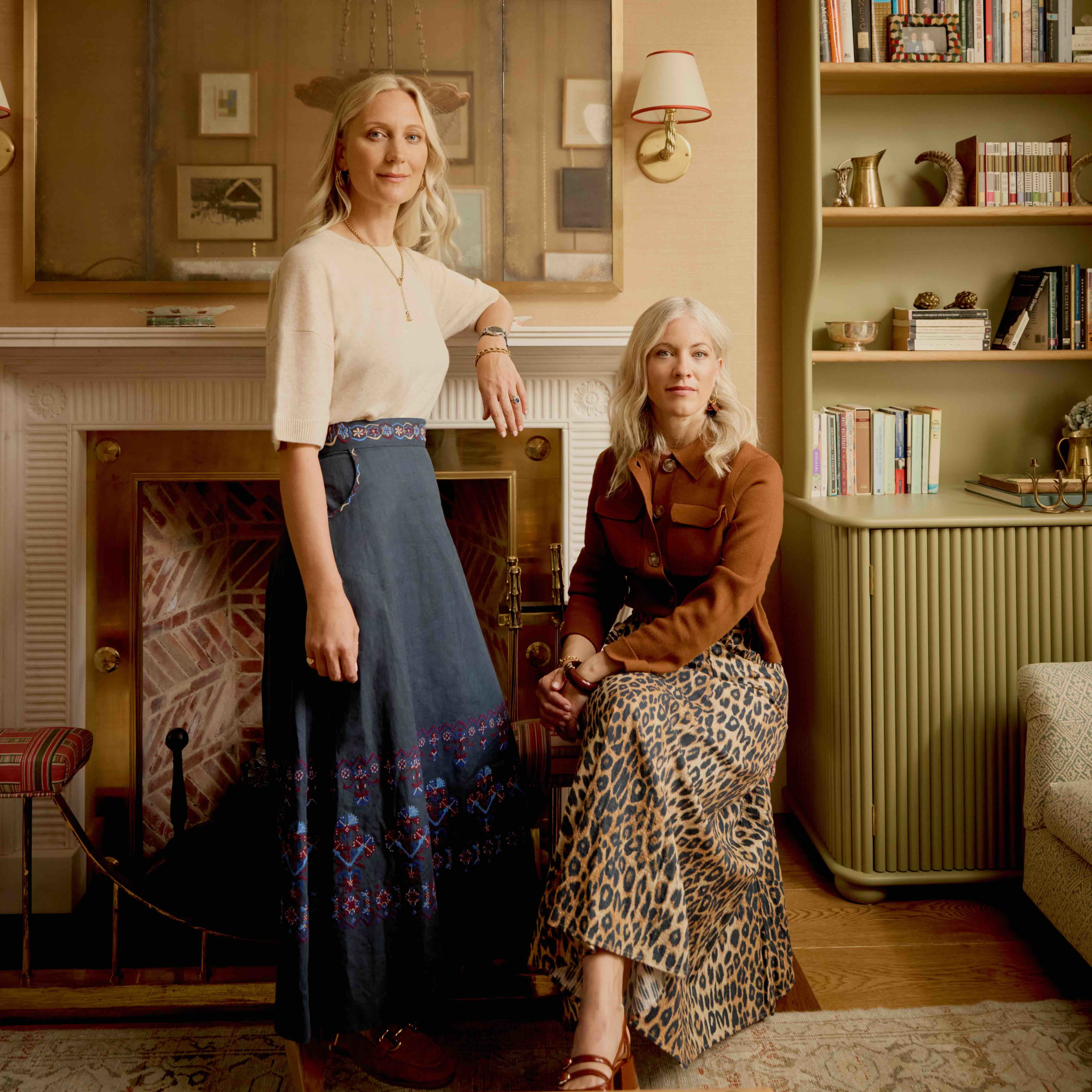 two women sitting in a living room next to a fireplace