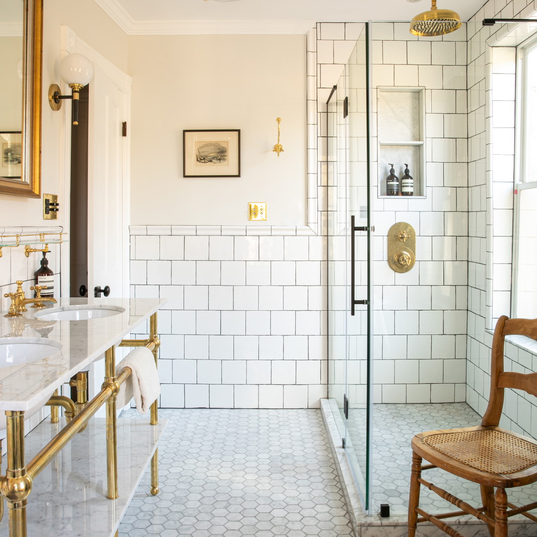 a white tiled bathroom with a wooden chair