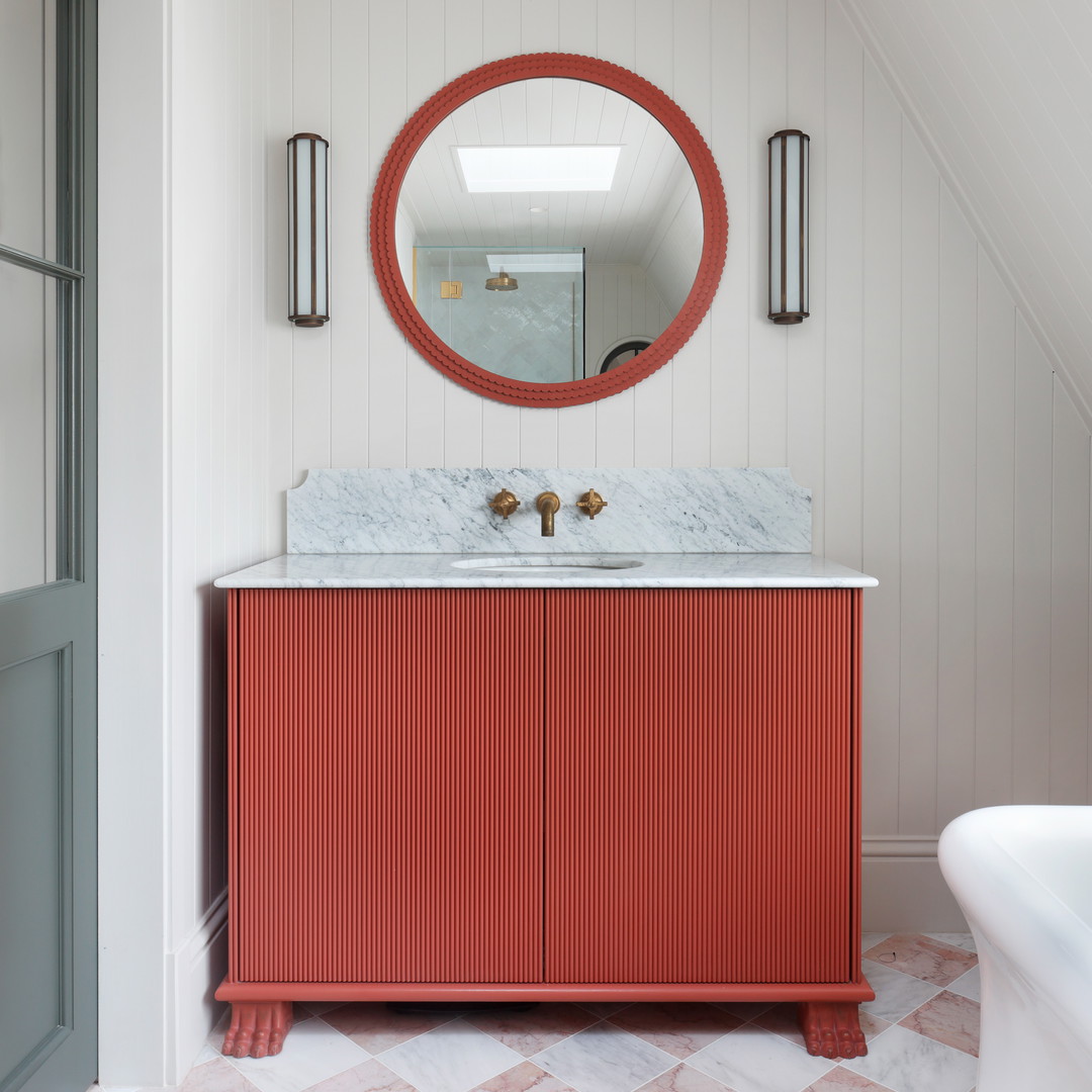 a bathroom with a red cabinet and a round mirror