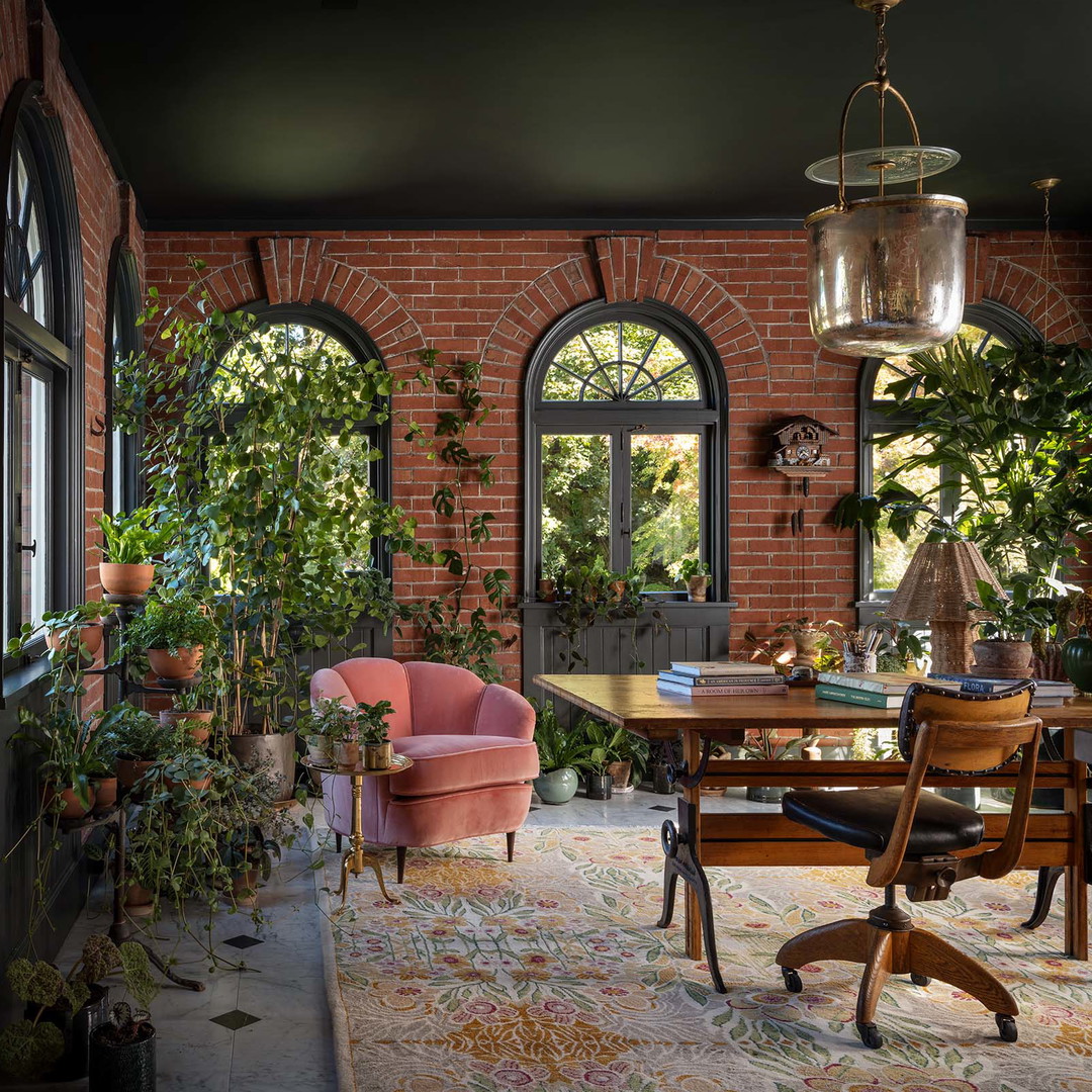 a room with a table, chairs, potted plants and windows