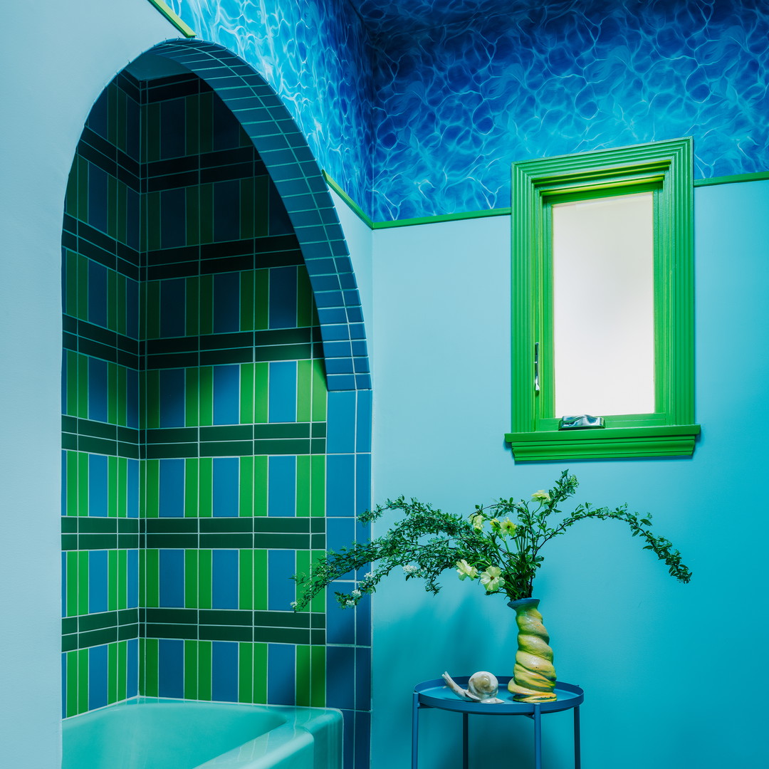 a blue bathroom with a green window and a tub