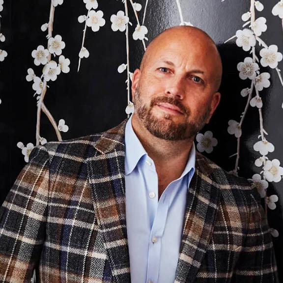 a man in a suit and tie standing in front of a floral wall