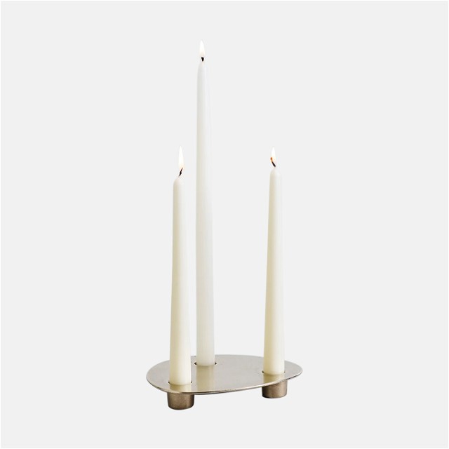 three white candles sitting on top of a metal stand
