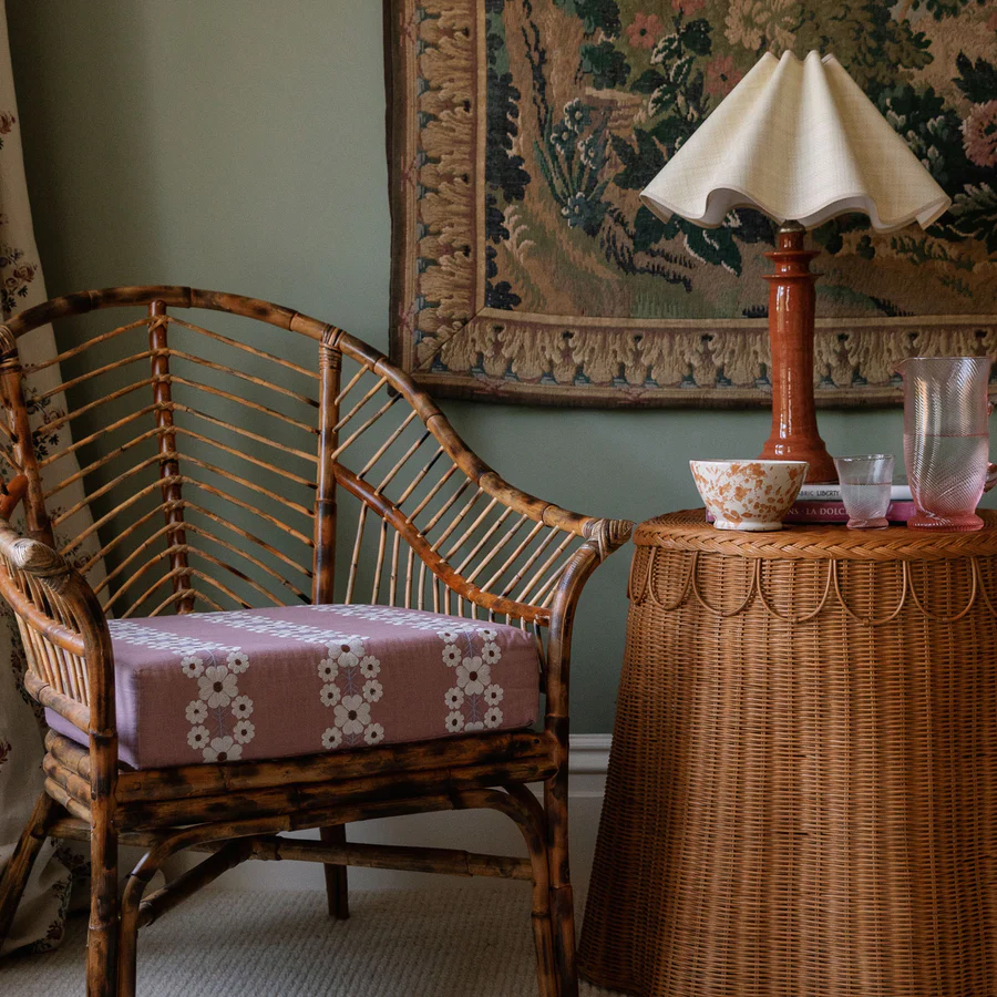 a wicker chair next to a table with a lamp on it