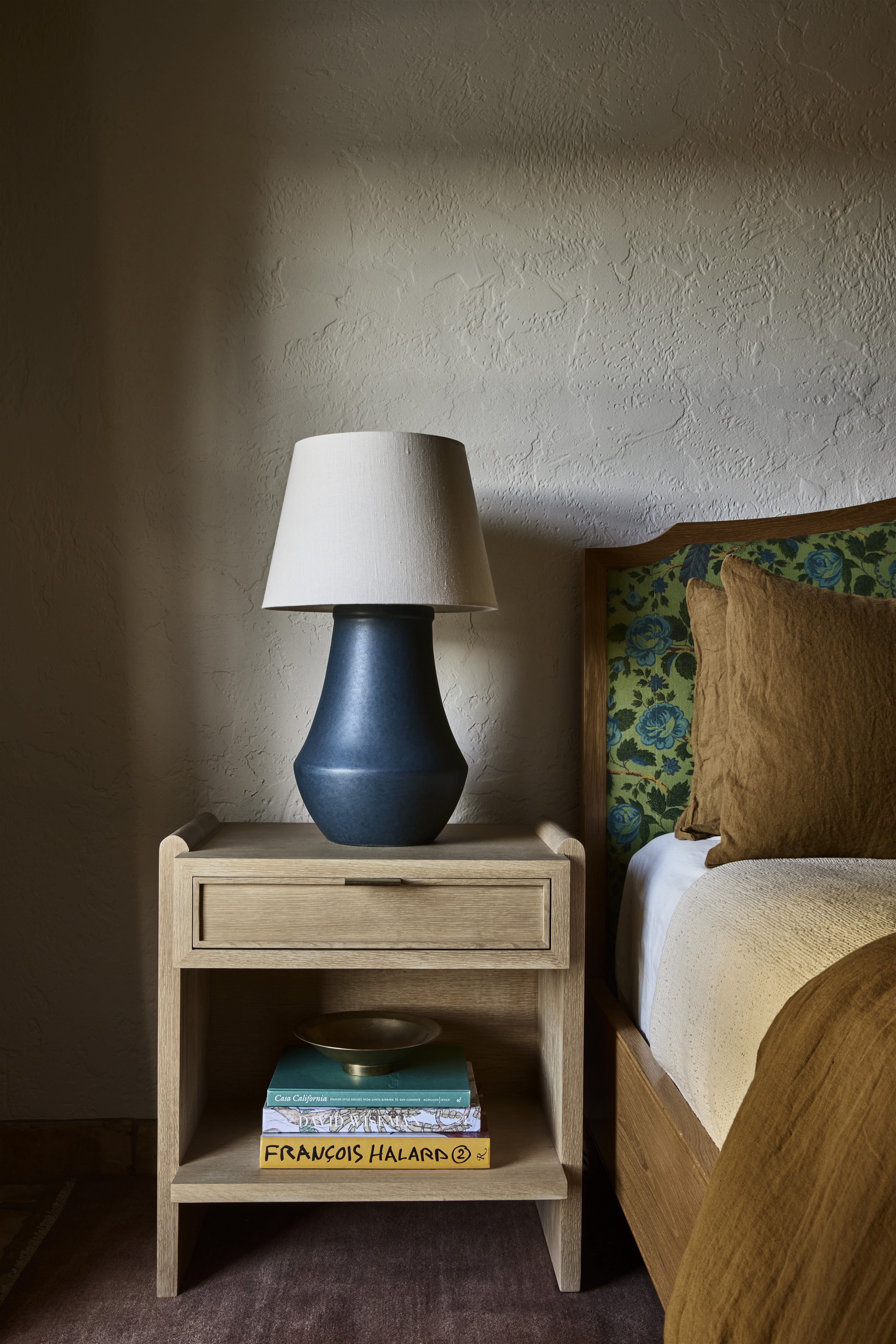 a nightstand with a lamp on top of it next to a bed