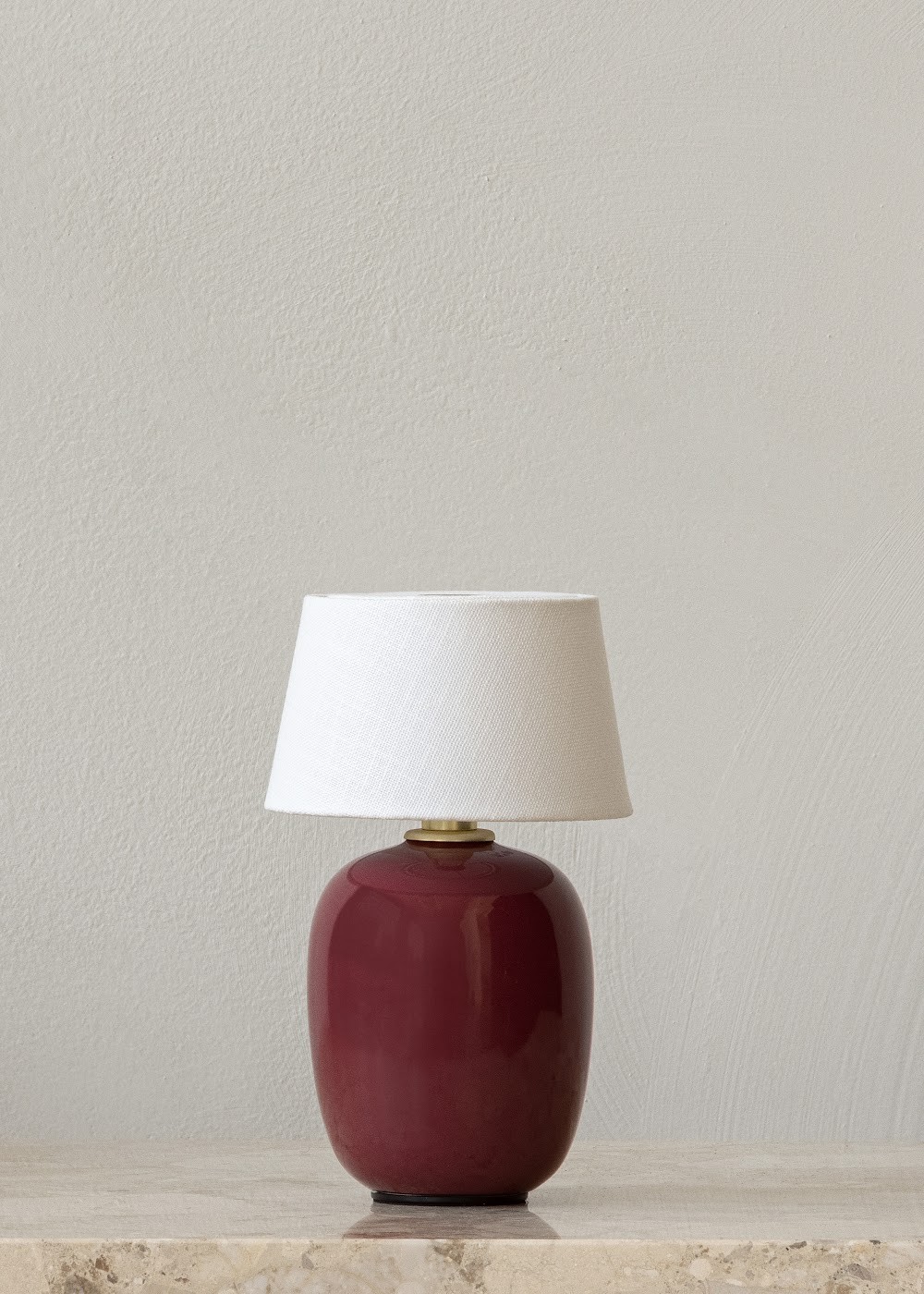 a red vase sitting on top of a table next to a white lamp