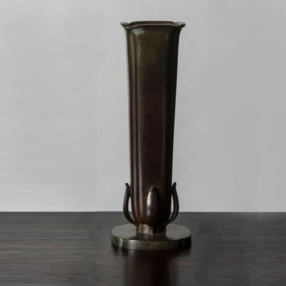a tall metal vase sitting on top of a wooden table