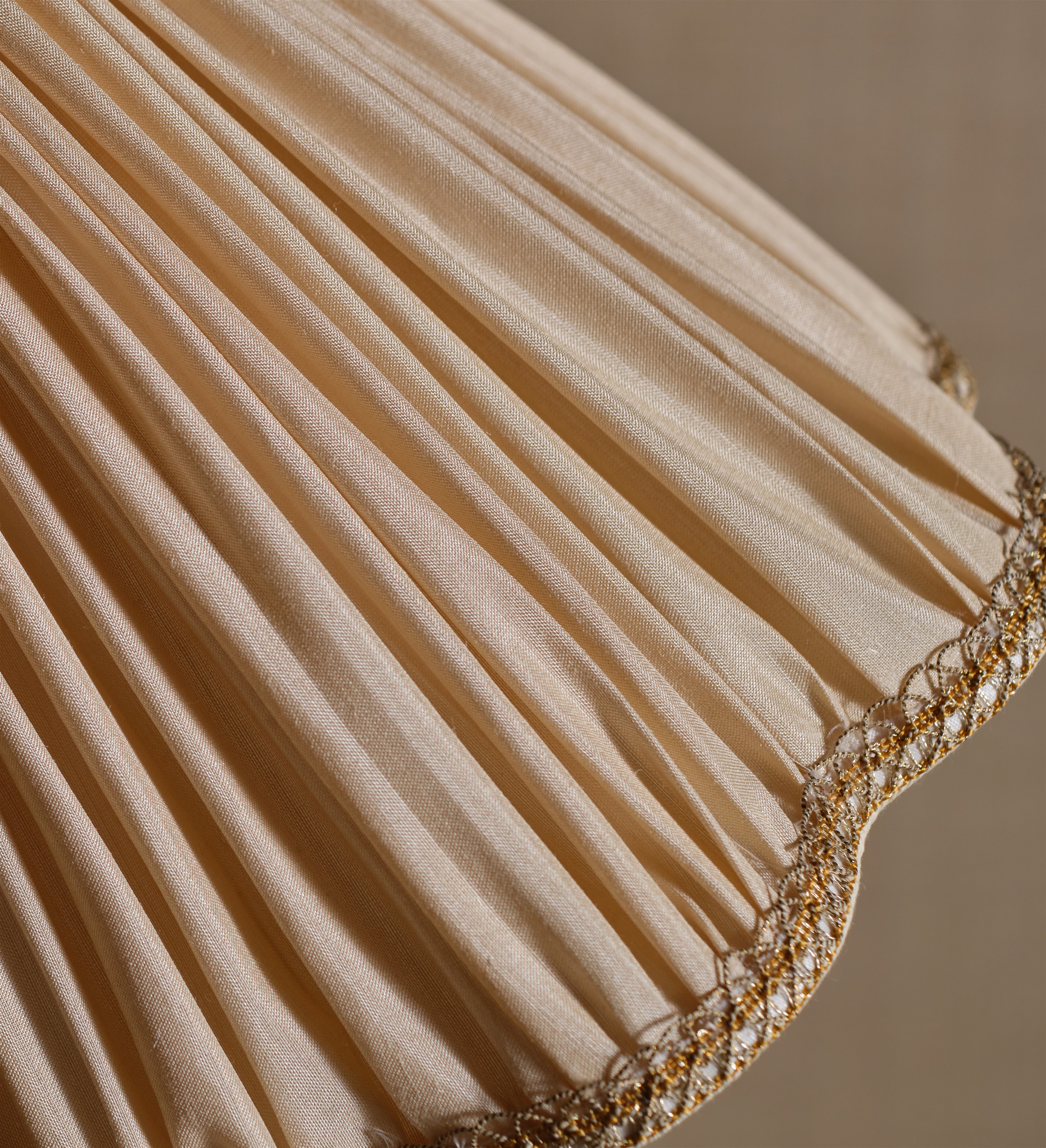 a beige pleated lamp shade with gold trim