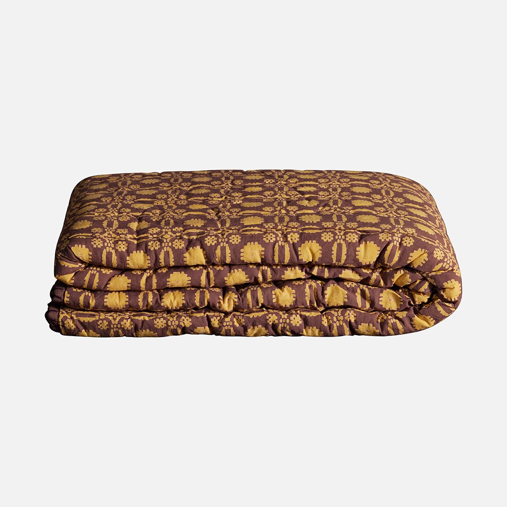 a bed with a brown and yellow comforter on top of it