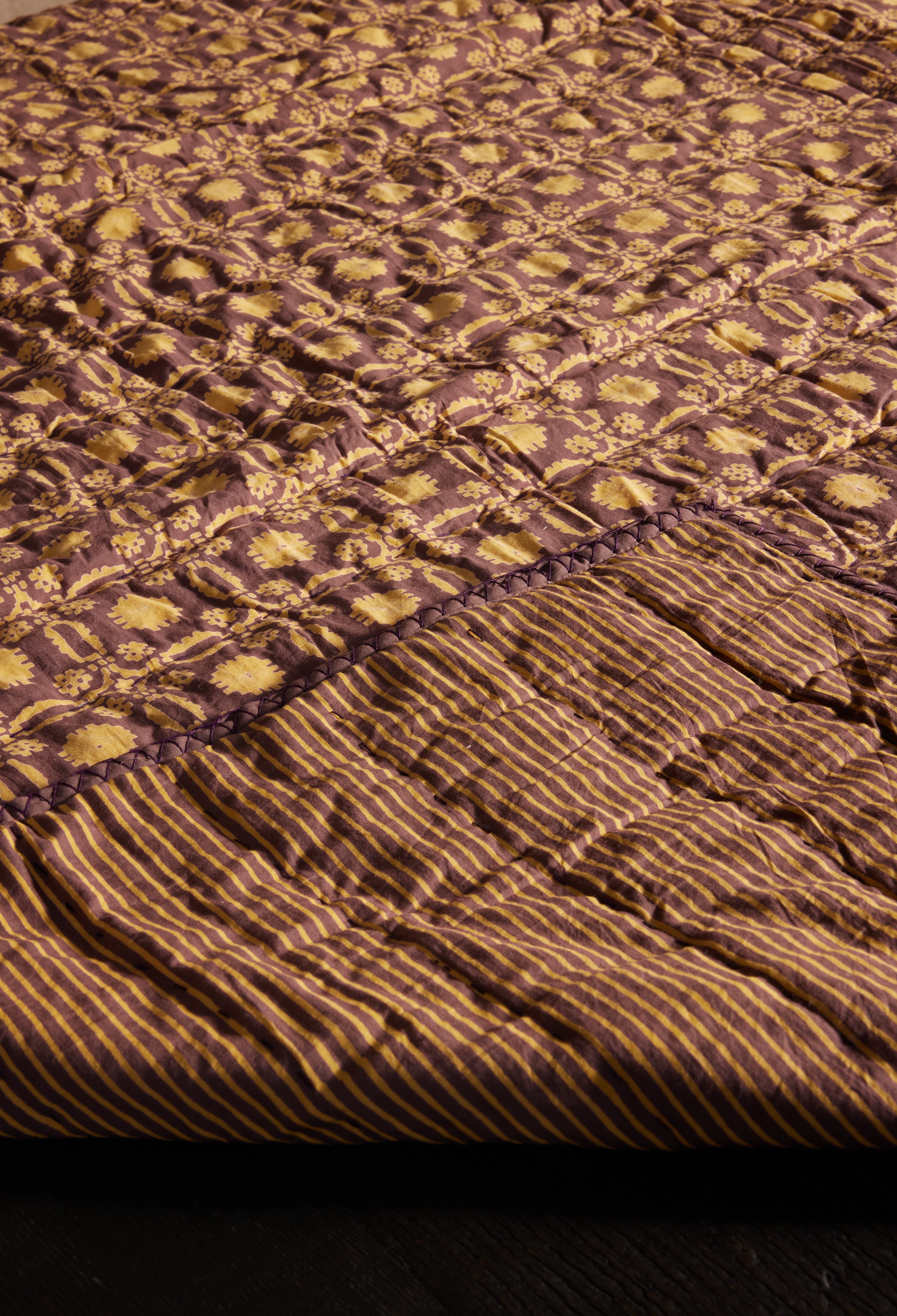 a bed with a purple and gold comforter on top of it