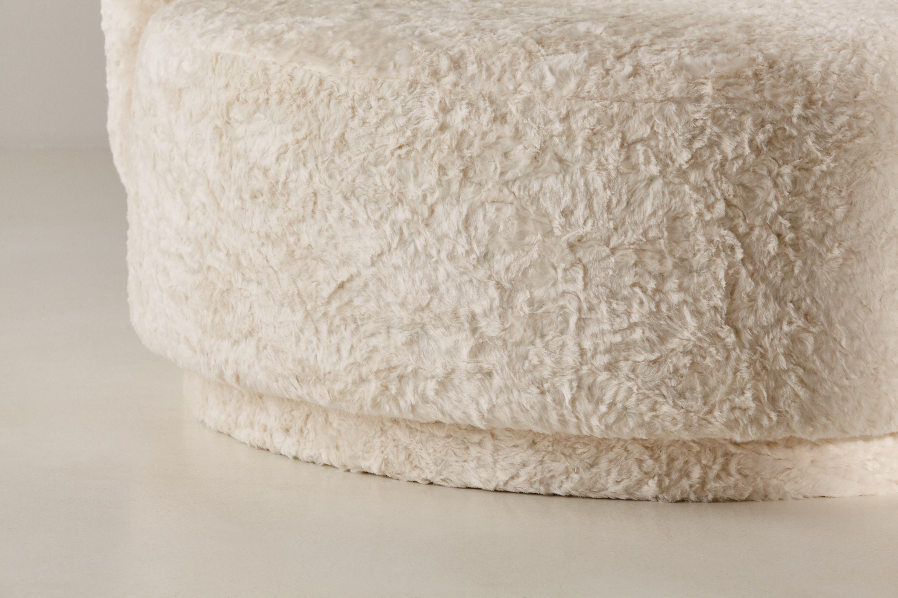 a large white round ottoman with a long pile of fur on top of it